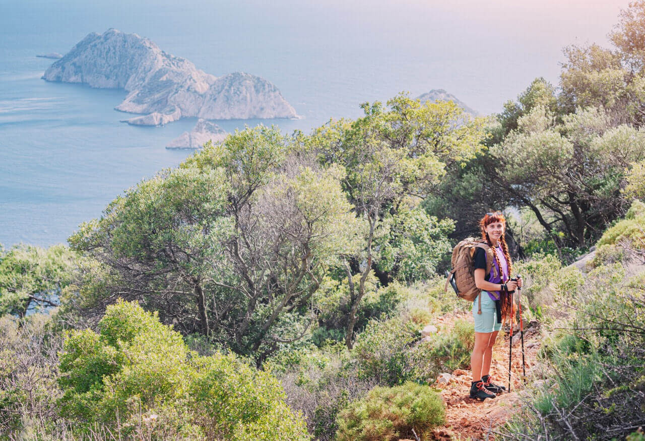 happy redhead hiker girl with trekking poles backpack walking by scenic lycian way path turkey along azure sea coast near gelidonya lighthouse Large