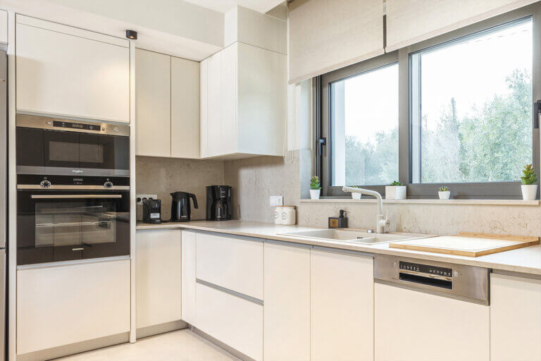 A sleek, modern kitchen with white cabinetry, stainless steel appliances, and a view of greenery through the window.