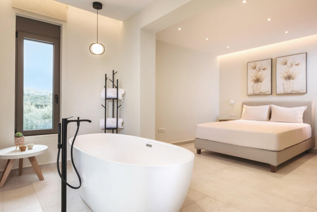 Bright and airy master bedroom ensuite with a modern bathtub, towel rack, and large window offering a view of rolling hills.