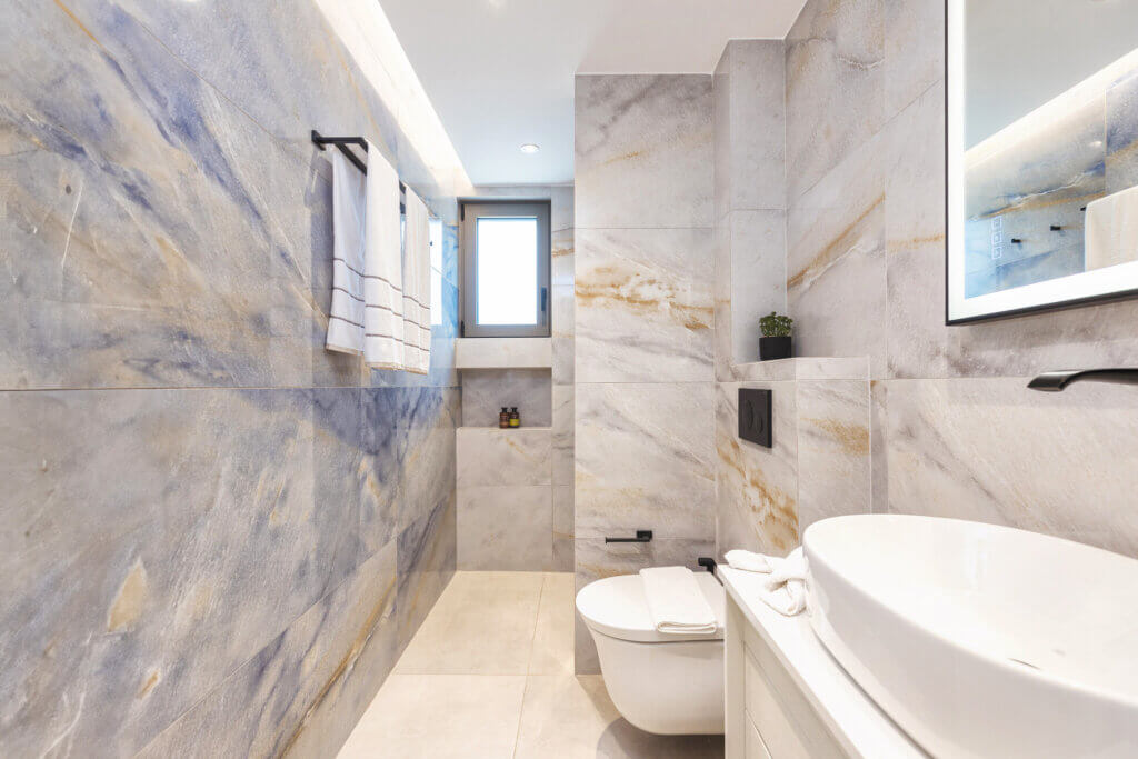 A sleek and contemporary master bathroom with marbled walls, and a walk-in shower, illuminated by natural light.