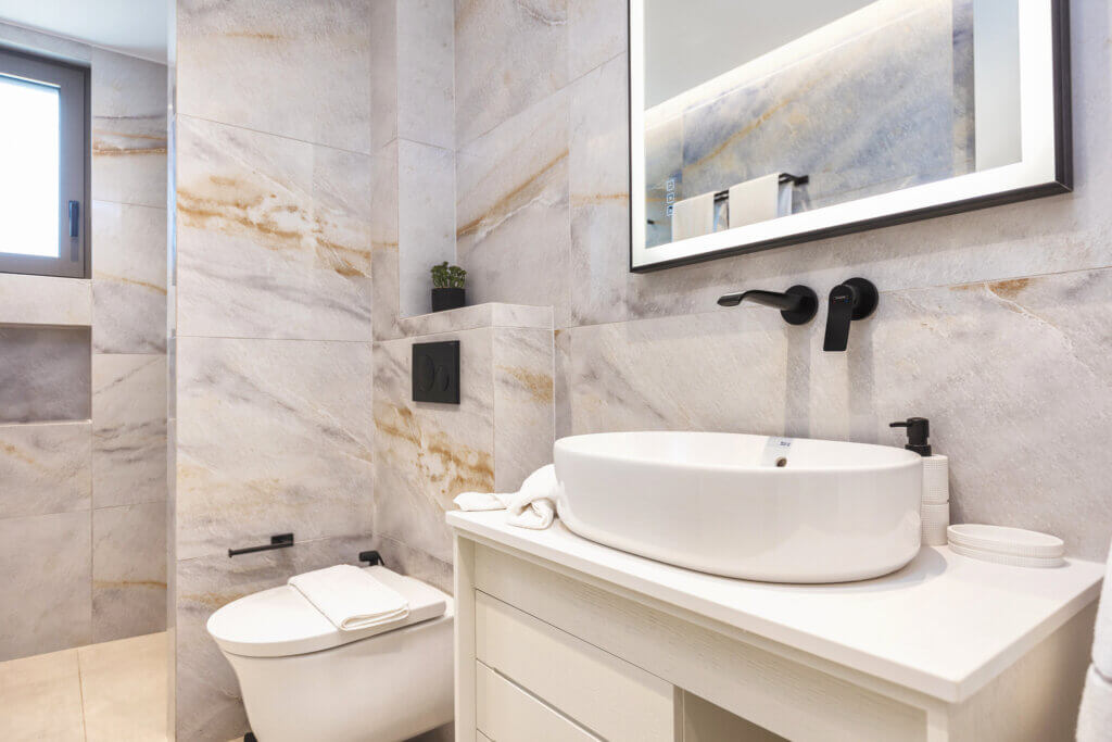 A sleek and contemporary master bathroom with marbled walls, and a walk-in shower, illuminated by natural light.