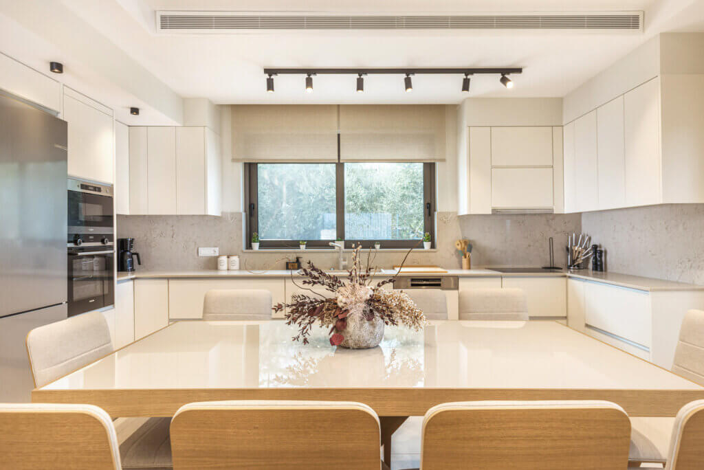 A sleek, modern kitchen with white cabinetry, stainless steel appliances, and a view of greenery through the window.