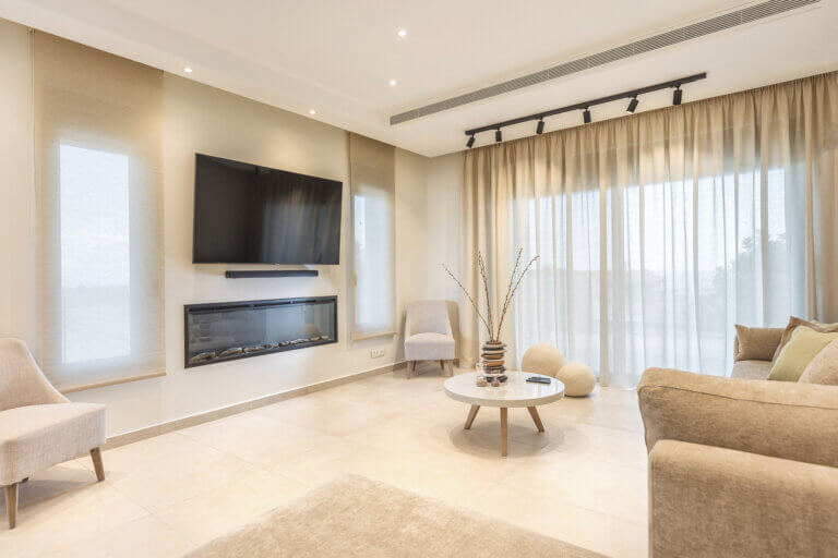 Mamfredas Luxury Residence A large living room with a beige sectional sofa, modern fireplace, wall-mounted TV, and elegant drapery.